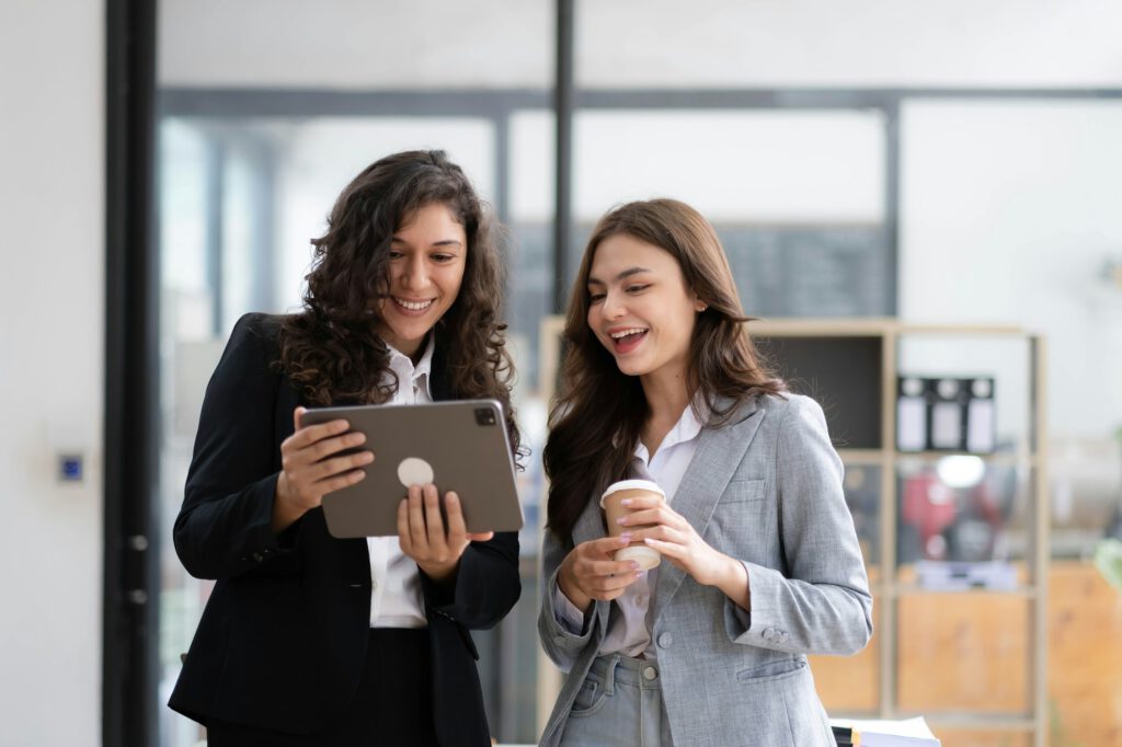 Two beautiful Asian businesswomen standing using digital tablet consulting and analyzing information