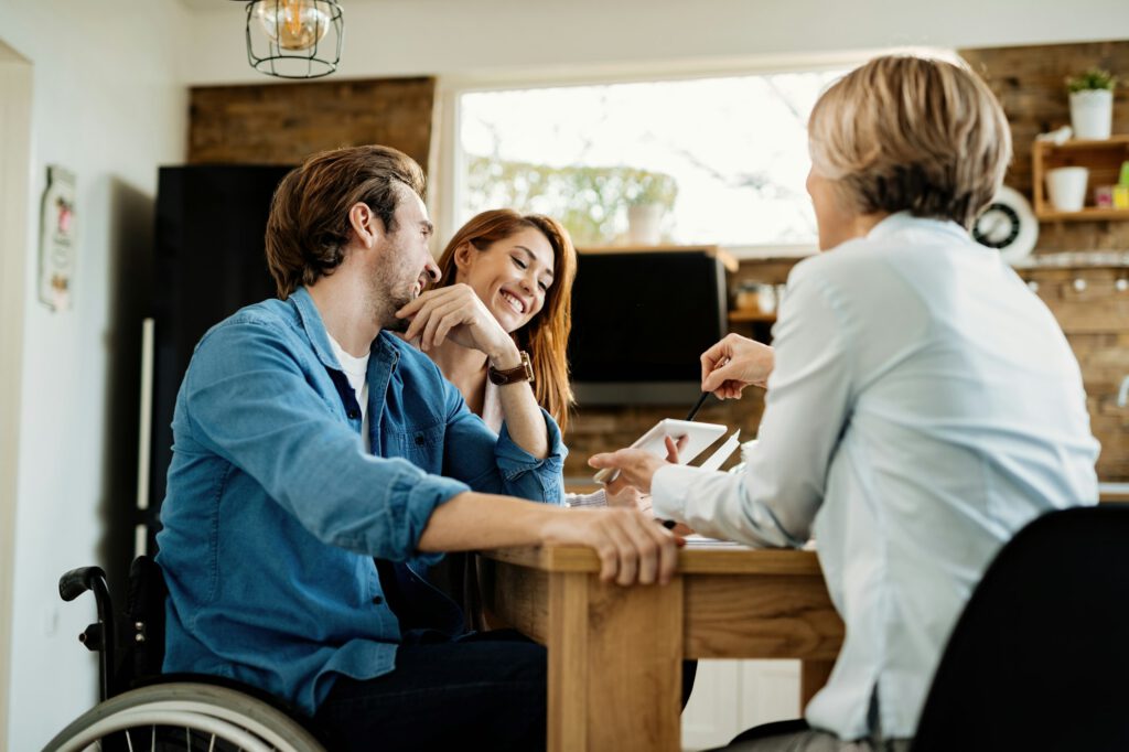 Young happy couple and their real estate agent using touchpad on a meeting at home.