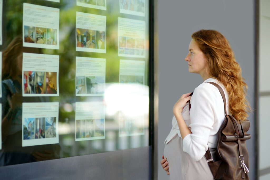 Young pregnant woman exploring storefront of real estate agency.